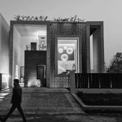 A dramatic black and white evening view of our "House of Frames" project, emphasizing its strong geometric volumes and the interplay of light. The design uses large openings and a perforated screen to create layers of transparency and privacy.