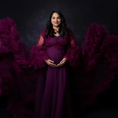 The full effect of this magnificent purple maternity gown, with its ruffled train spread out to create a sense of drama and elegance. This is a perfect example of a show-stopping studio maternity shot.