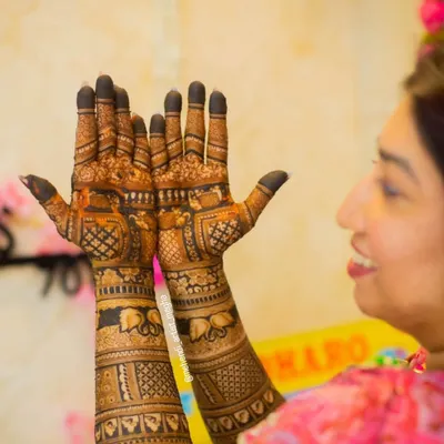 A lovely candid moment of a bride admiring her intricate mehendi. The design features traditional elements like peacocks, lotuses, and elephants.