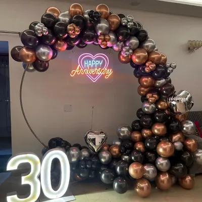 Mark a special milestone like a 30th anniversary with a sophisticated decoration. This setup features a modern balloon arch in black, silver, and bronze, a 'Happy Anniversary' neon sign, and large light-up '30' numbers.