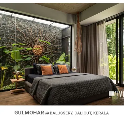 The master bedroom at Gulmohar is a true retreat, with a full-length glass wall opening to a private courtyard and a stunning sun-ray art piece on a natural stone wall.