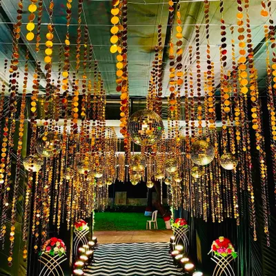A dazzling entrance tunnel designed for a Sangeet night. The ceiling is covered with hanging strings of golden sequins and multiple disco balls, creating a shimmering, immersive experience for guests as they walk in.
