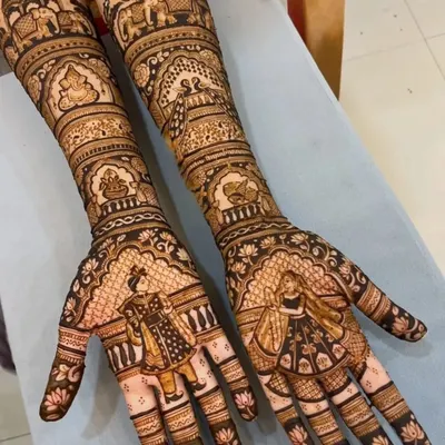 A stunning full bridal design with detailed bride and groom figures on the palms. The arms are covered in traditional wedding scenes, including palanquins and elephants, for a truly narrative-driven mehndi.