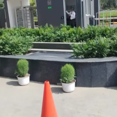 A formal and structured entrance design for a corporate facility. The combination of a manicured hedge within a stone planter and uniform potted shrubs creates a clean, professional, and welcoming first impression.