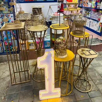 I offer a wide range of party props for rent to complete your event's look. This photo shows some of my inventory, including gold-finished cake stands, decorative plinths, and a large light-up number '1', perfect for first birthdays or anniversaries.