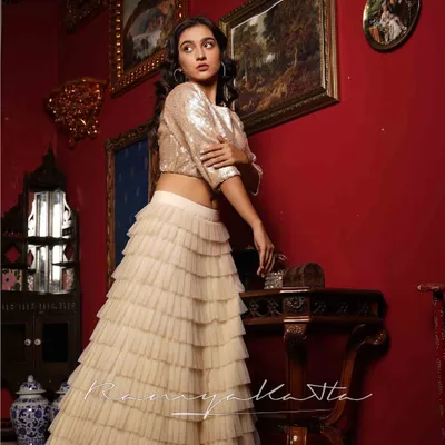 A glamorous ensemble perfect for a cocktail party or sangeet. The shimmering beige sequin crop top is paired with a multi-layered tulle frilled lehenga for a dramatic and modern look.