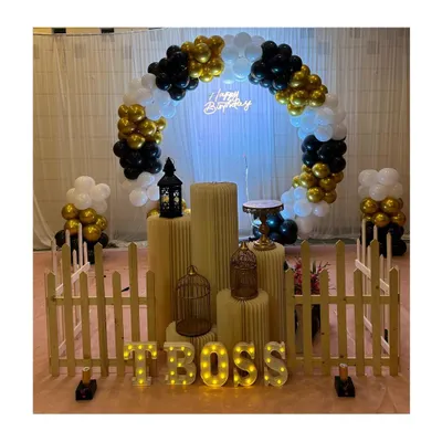 A chic and modern birthday setup with a black, white, and gold color scheme. The decor features a circular balloon arch, a neon sign, and a small picket fence for a stylish touch.