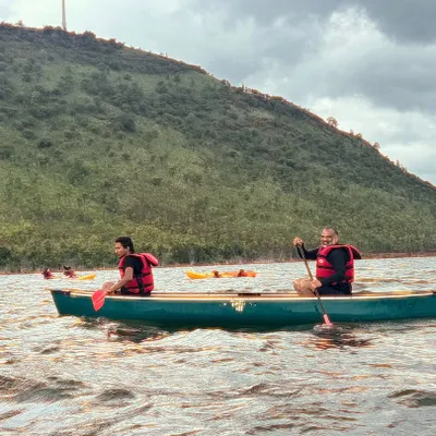 Participants enjoy a peaceful canoeing session on the waters of Vani Vilas Sagar, with the green hills providing a beautiful backdrop.
