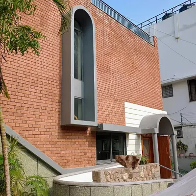The facade of the Brick Vault House in Hyderabad, showcasing the adaptive reuse of the original structure. The design combines exposed brick with modern arched windows and a new water feature, creating a distinctive ethno-modern aesthetic.