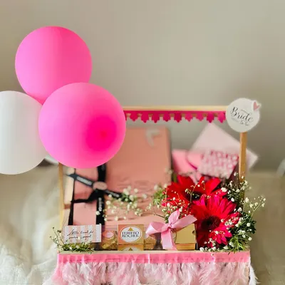 A vibrant and celebratory 'Bride to be' hamper, perfect for a bachelorette party or bridal shower. It's decorated with pink feathers, balloons, and fresh flowers for a fun, festive look.