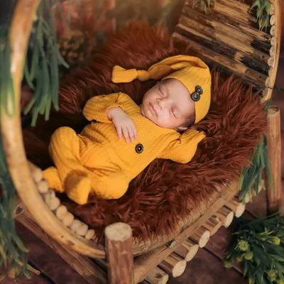 A perfect example of a classic newborn pose. This little one is sleeping peacefully in a rustic, circular wooden prop, dressed in a cozy yellow outfit that contrasts beautifully with the rich, warm tones of the setup.