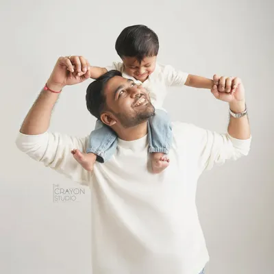 The view from dad's shoulders is always the best. This studio portrait captures the pure joy and laughter between a father and son, set against a simple white background to let their connection shine.