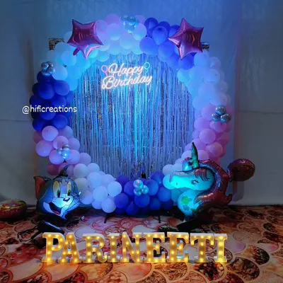A fun and colorful setup for a young fan of cartoons. This party decoration combines a Tom & Jerry foil balloon with a unicorn theme, set against a circular balloon backdrop with a silver shimmer curtain and the name 'PARINEETI' in marquee letters.