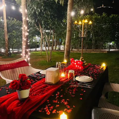 An example of a romantic outdoor dinner for two. I handle the complete table arrangement, including a table runner, scattered rose petals, a candelabra centerpiece, and ambient lighting from LED candles and overhead string lights for a private, cozy atmosphere.