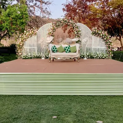A beautiful day wedding stage with a modern white slatted backdrop, adorned with white and green floral arrangements. The vintage sofa adds a touch of classic elegance.
