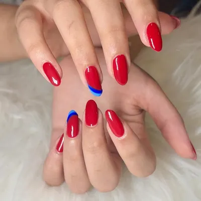 A classic red manicure with a twist. This set features glossy, almond-shaped red nails with a surprise abstract swipe of bright blue on two accent nails.