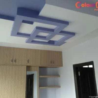 A bold, interlocking geometric false ceiling design in a two-tone color scheme. This POP construction adds a strong visual focus to the bedroom and complements the existing wooden wardrobes.