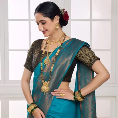 A model adorned in a full traditional Maharashtrian jewellery set, including a long haar and nath. The shot is framed to highlight the detailed craftsmanship against a vibrant blue silk saree, perfect for a bridal catalogue.