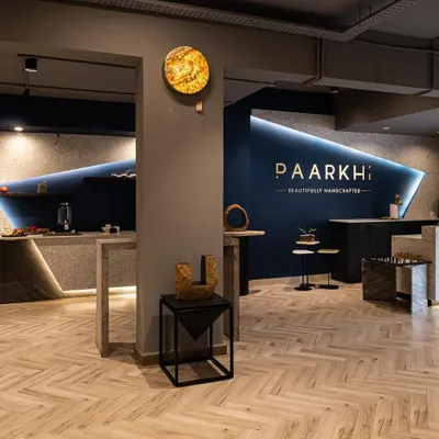 An overall view of the Paarkhi boutique, showing how the reception area and bar section were designed to mirror each other. The signature 'Paarkhi blue' wall with gold branding serves as a powerful anchor for the entire space.