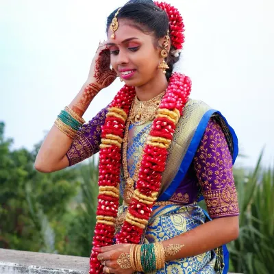 A joyful, candid moment during a puberty ceremony photoshoot. Her genuine smile and traditional attire, complete with a beautiful flower garland, are captured perfectly against the natural outdoor light.