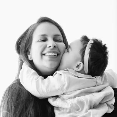 An emotional black and white image of a baby giving her mother a sweet kiss on the cheek.