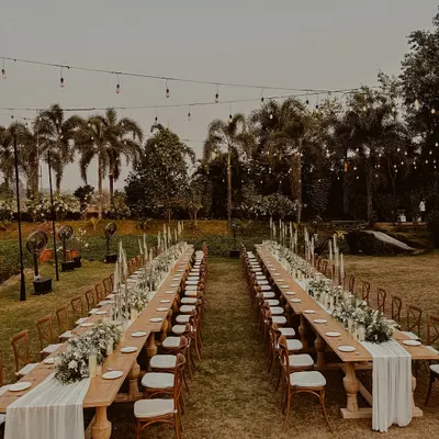 A breathtaking view of our long-table sit-down dinner setup. The combination of rustic wooden tables, a full floral runner, and a canopy of fairy lights creates an atmosphere of pure enchantment.