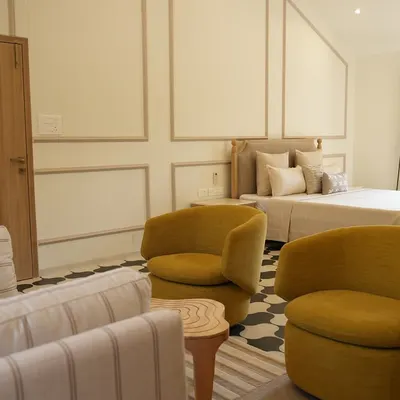The master bedroom of an Alibaug villa, designed to be a breath of calm. The combination of neutral wall mouldings, a comfortable striped sofa, and bold mustard armchairs creates a space that is effortlessly luxurious.