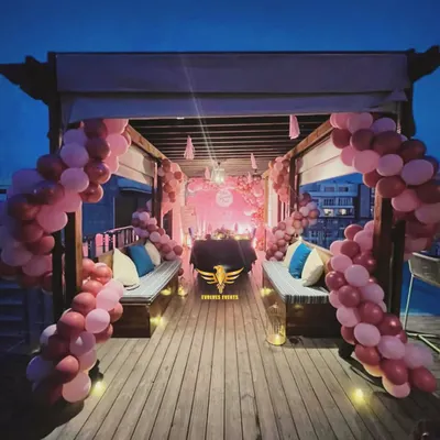 A beautiful rooftop candlelight dinner setup. The decor features a cabana draped with pink balloon arches, creating a private and romantic dining experience under the stars.