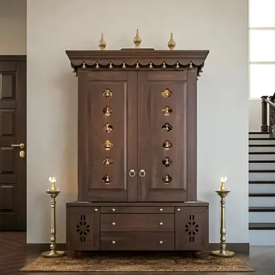 A magnificent, traditional freestanding pooja unit crafted from dark wood. This mandir features ornate carvings, temple bells on the doors, and a decorative top, creating a grand and sacred presence in the home.