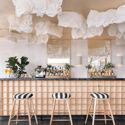 The bar at Brassa features a light wood grid base and bold, black-and-white striped stools. Above, a custom installation of fabric origami lights adds a soft, sculptural element to the ceiling.