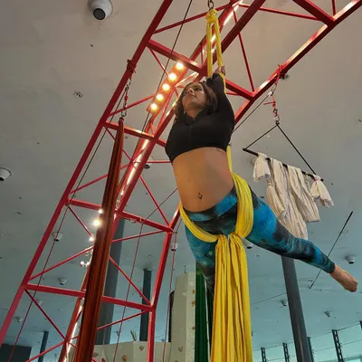 An aerialist hangs suspended from yellow silks, demonstrating the core strength and balance central to our silks classes.