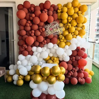 A stunning balloon wall created for a birthday party. This backdrop features a mix of rust, mustard, white, and chrome gold balloons in various sizes for a textured, organic look.