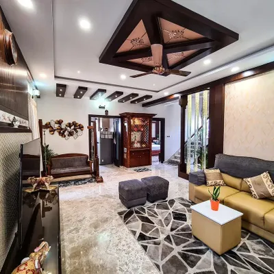 This is a wide view of a family living area where I used marble flooring and a mix of ceiling styles to define the space. The layout includes a comfortable L-shaped sofa, a traditional wooden jhoola, and a glimpse of the ornate pooja mandir, creating a harmonious blend of functions.