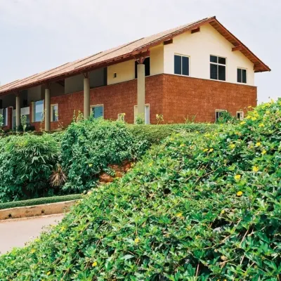 The "Office in a Verandah" in Goa is defined by its large, sheltering roof and laterite base, designed to withstand and celebrate the region's heavy rainfall. The building sits comfortably in its lush, hilly landscape.