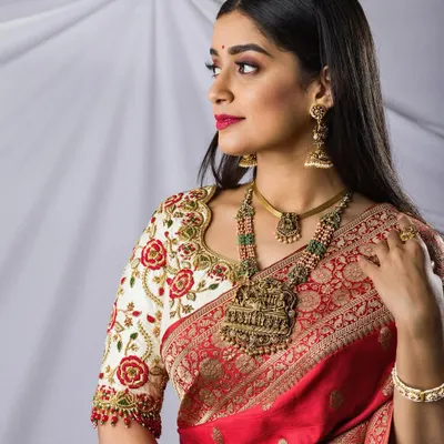 A stunning bridal portrait in a vibrant red saree, showcasing antique temple jewelry and an intricately embroidered blouse. A perfect blend of tradition and elegance.