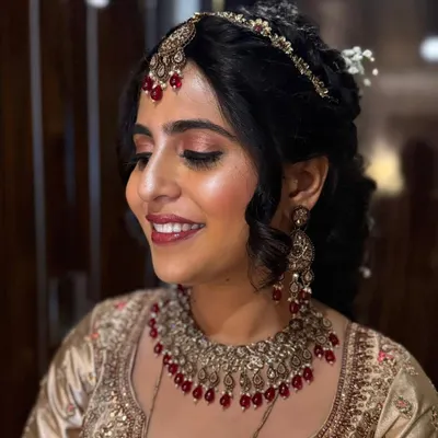 A glowing bride ready for her wedding ceremony. Her look features a soft, romantic updo with intricate braids and a traditional matha patti, paired with radiant makeup that enhances her natural features.