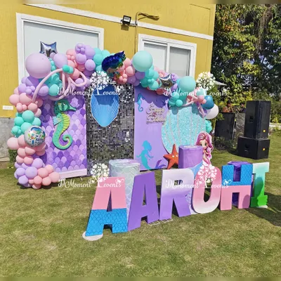 An amazing outdoor mermaid-themed stage, complete with a sequin wall, custom marquee letters, and props of various sea creatures, all set up on a sunny lawn.