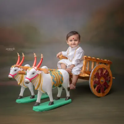 A charming portrait of a baby boy in a simple white kurta, sitting on a miniature bullock cart. This theme captures the essence of rural Maharashtrian culture.