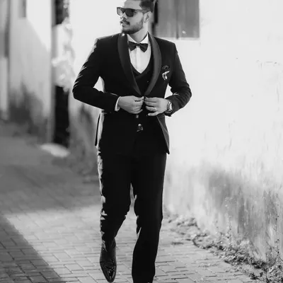 A classic black and white shot of the groom, looking sharp and confident in his tuxedo as he walks down a sunlit alley.