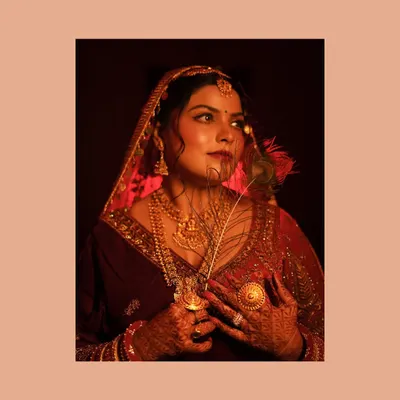 This close-up bridal portrait is all about mood and detail. The warm, dramatic lighting highlights the rich color of her velvet lehenga and the intricate gold jewelry. The peacock feather adds an artistic, symbolic touch to this couture bridal shot.