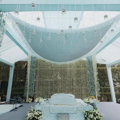 A serene and elegant setup for an Anand Karaj ceremony. The design features a soft powder blue and white color palette, with a stunning ceiling installation of cascading white flowers creating a divine canopy.