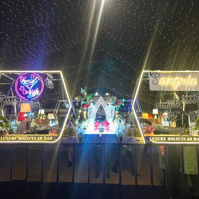 A panoramic view of our dual-station bar setup, designed to be a stunning centerpiece. Featuring custom hexagonal frames, neon signs for 'Cocktails' and 'Sangria', and a ceiling of fairy lights, this bar commands attention from every angle.