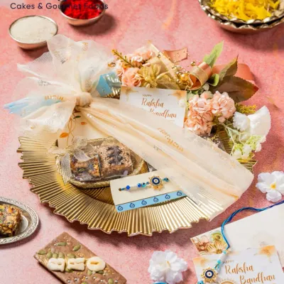 My Pooja Thali Rakhi Gift Hamper has everything your sibling needs. It includes brownies, a nut bar, mithai, and an Evil Eye Rakhi, all beautifully arranged on a golden platter.