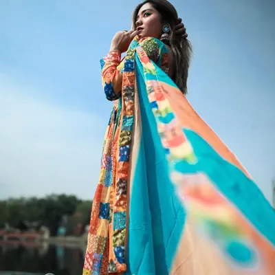 A beautiful shot of a model in a multi-colored Anarkali, with her dupatta flowing in the wind on a boat at Yamuna Ghat.