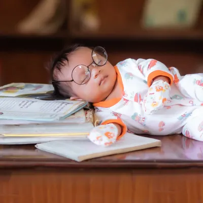 A sleepy little scholar. This creative newborn setup features a baby peacefully napping on a stack of books, complete with adorable oversized glasses.