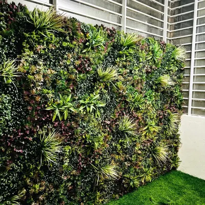 A close-up of one of our premium vertical garden walls. We use a variety of artificial plants with different textures, shapes, and shades of green and purple to create a dense, realistic, and visually interesting surface.