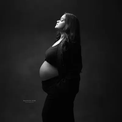 A powerful and classic black and white profile shot. The lighting beautifully sculpts the baby bump, creating a strong and timeless image of motherhood.