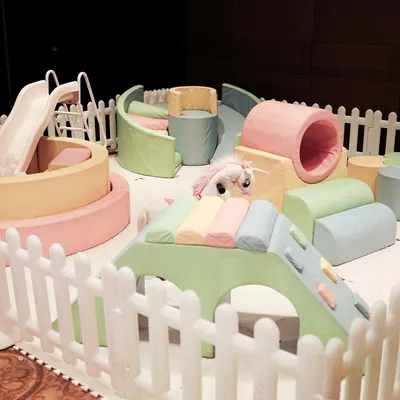 A dedicated soft play area for toddlers, set up with a ball pit, slide, and cushioned climbing structures, all enclosed by a white picket fence for safety.