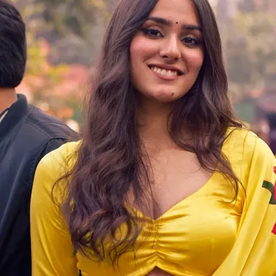 A natural and relaxed portrait of a woman in a vibrant yellow saree. The soft, diffused outdoor light and her comfortable smile make for an authentic and beautiful candid shot.