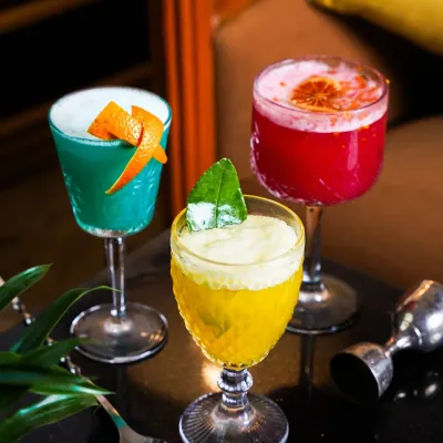 A trio of colorful cocktails, including a blue curaçao drink, a vibrant red concoction, and a frothy yellow sour, styled for a moody bar setting. This shot is perfect for showcasing a diverse cocktail menu.